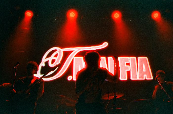 La banda en vivo frente al cartel de neón T. Maffia